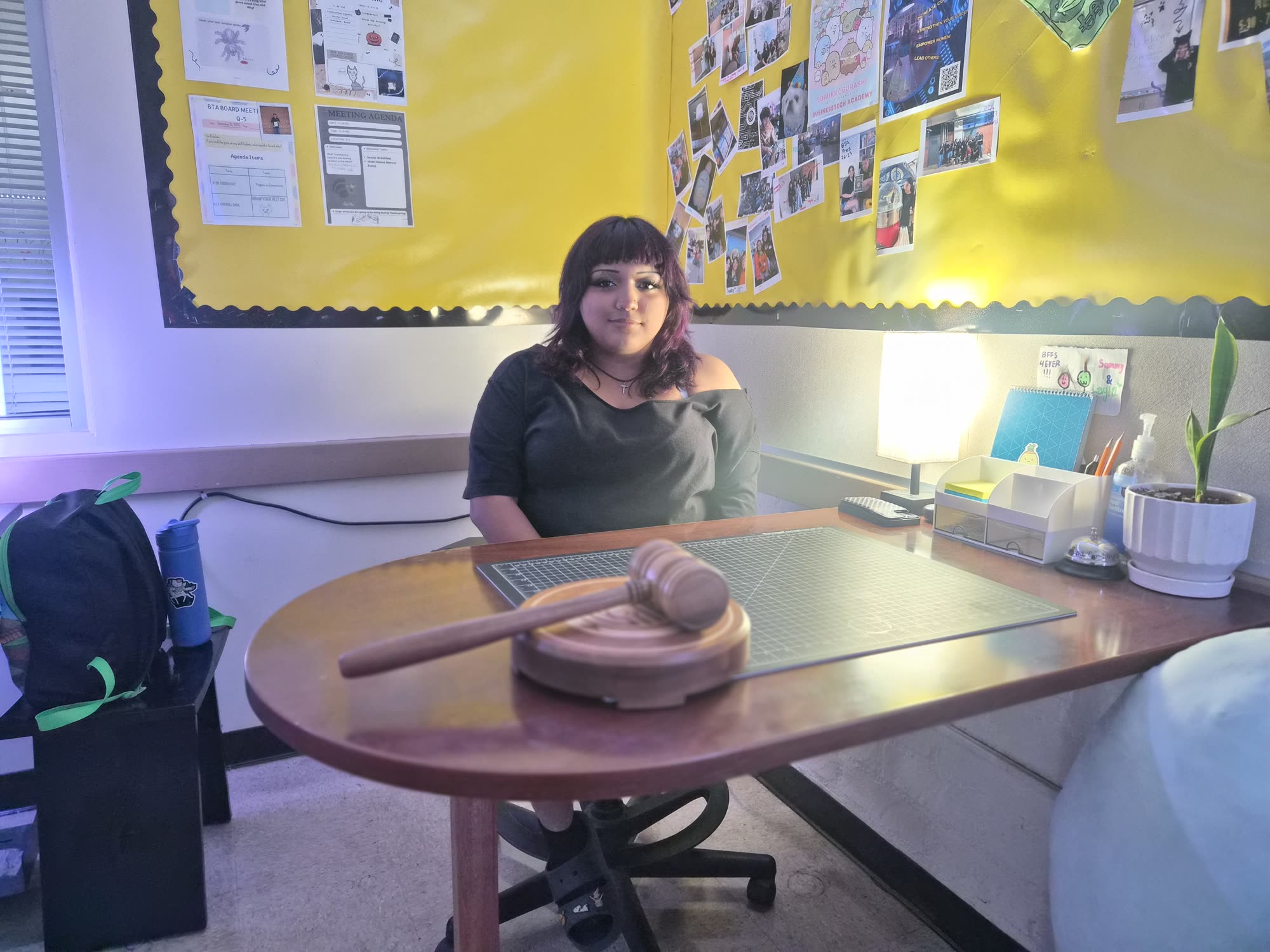 A student at the Academy Board table with the gavel, the meeting agenda pinned on the wall behind
