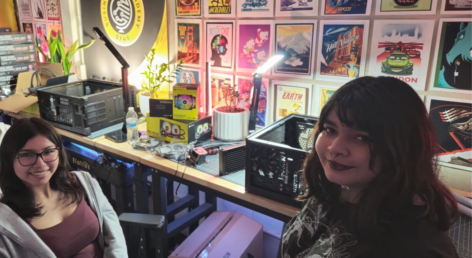 Two students at the build bench, the Academy seal and a wall of framed posters behind them