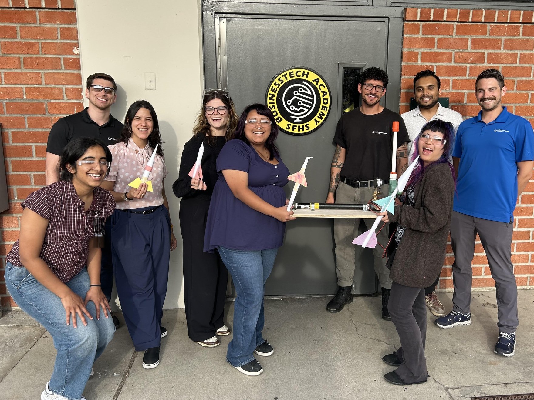 The student crew and the Collins Aerospace engineers who worked alongside them, holding the rockets they built