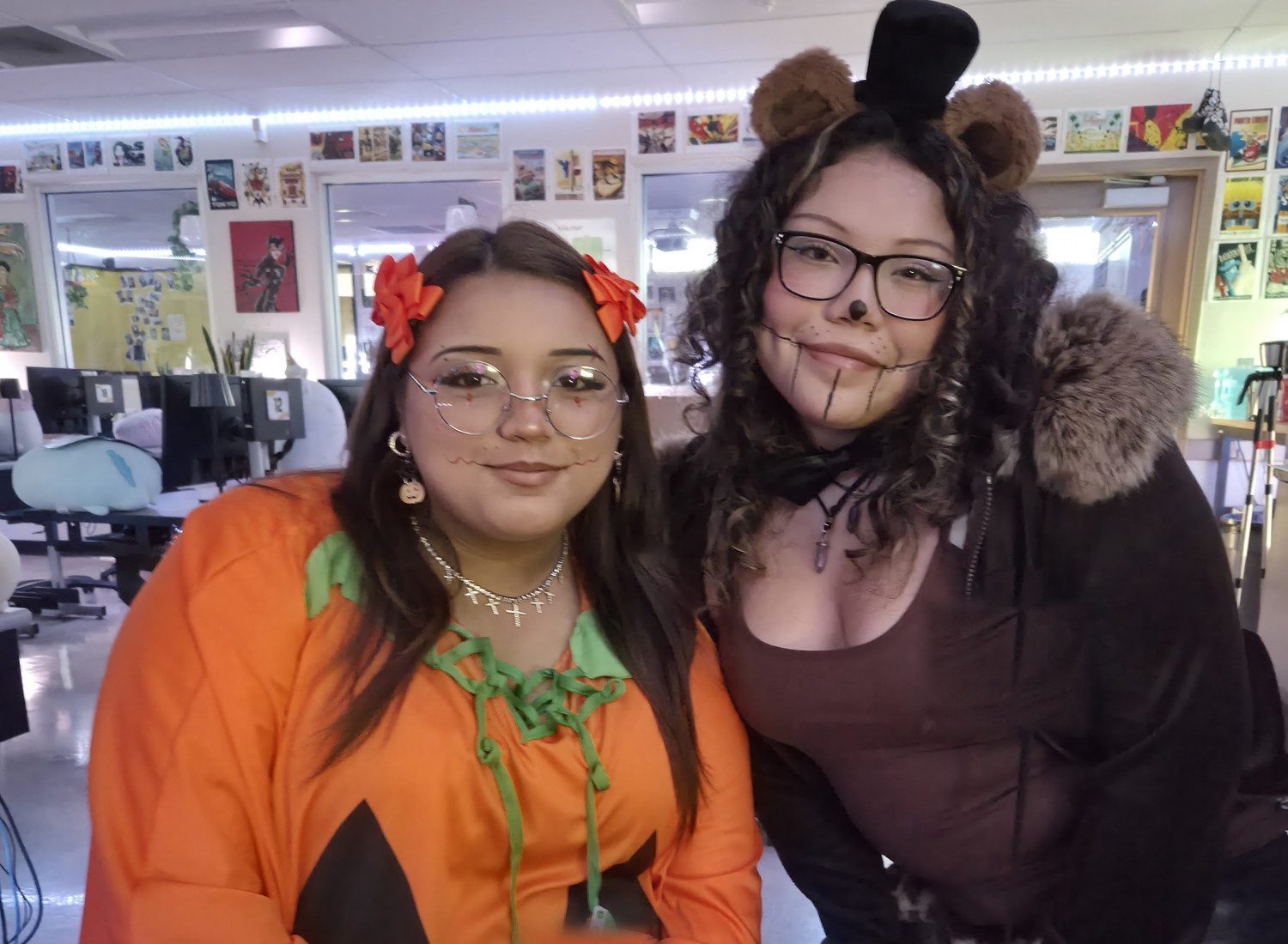 Two students in Halloween costume in the Academy room, one in a jack-o-lantern dress and one in bear ears