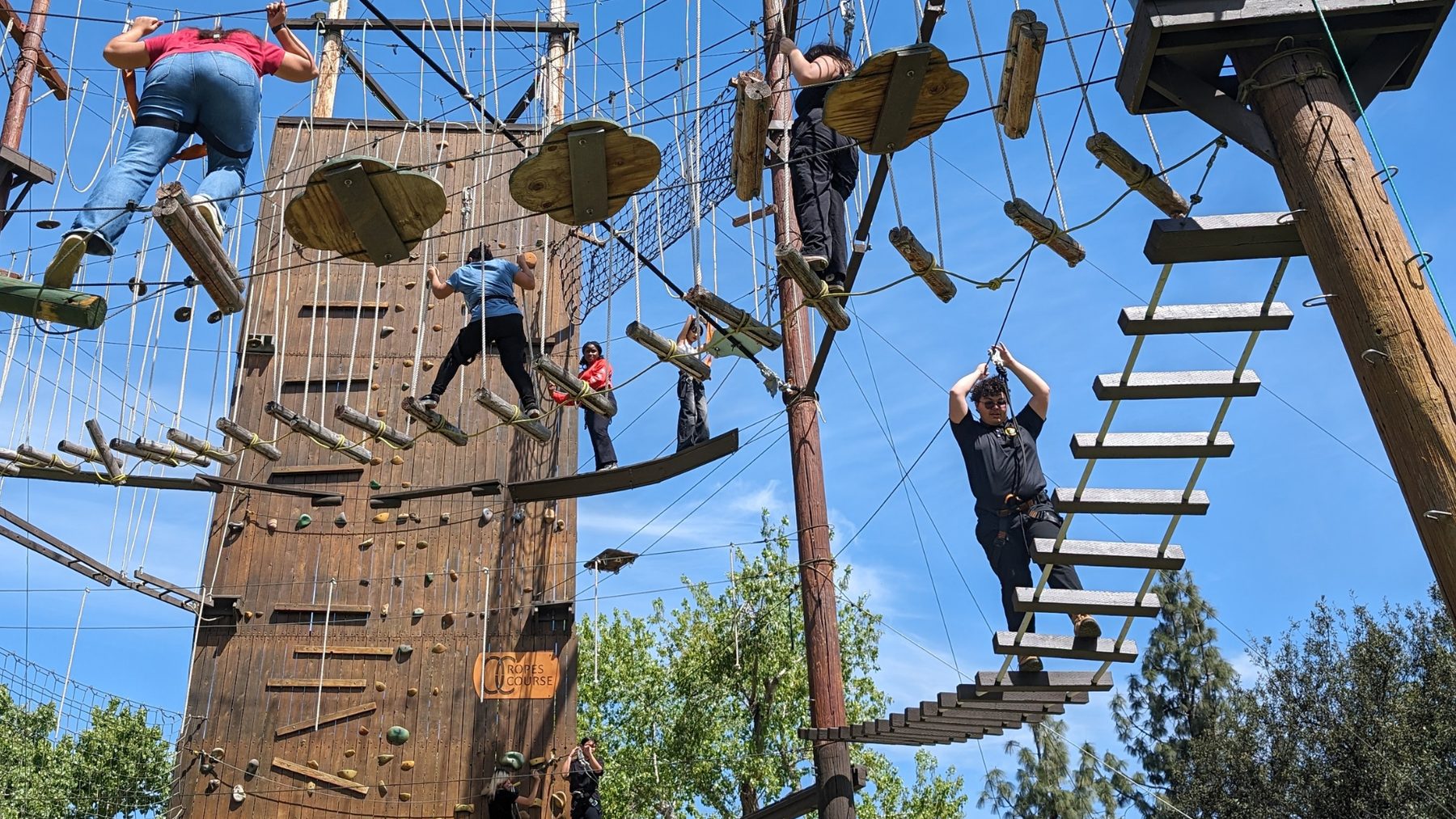 Academy students spread across a ropes-course tower against open sky